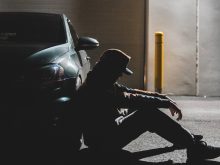 anonymous sad man sitting on ground near parked contemporary car in evening
